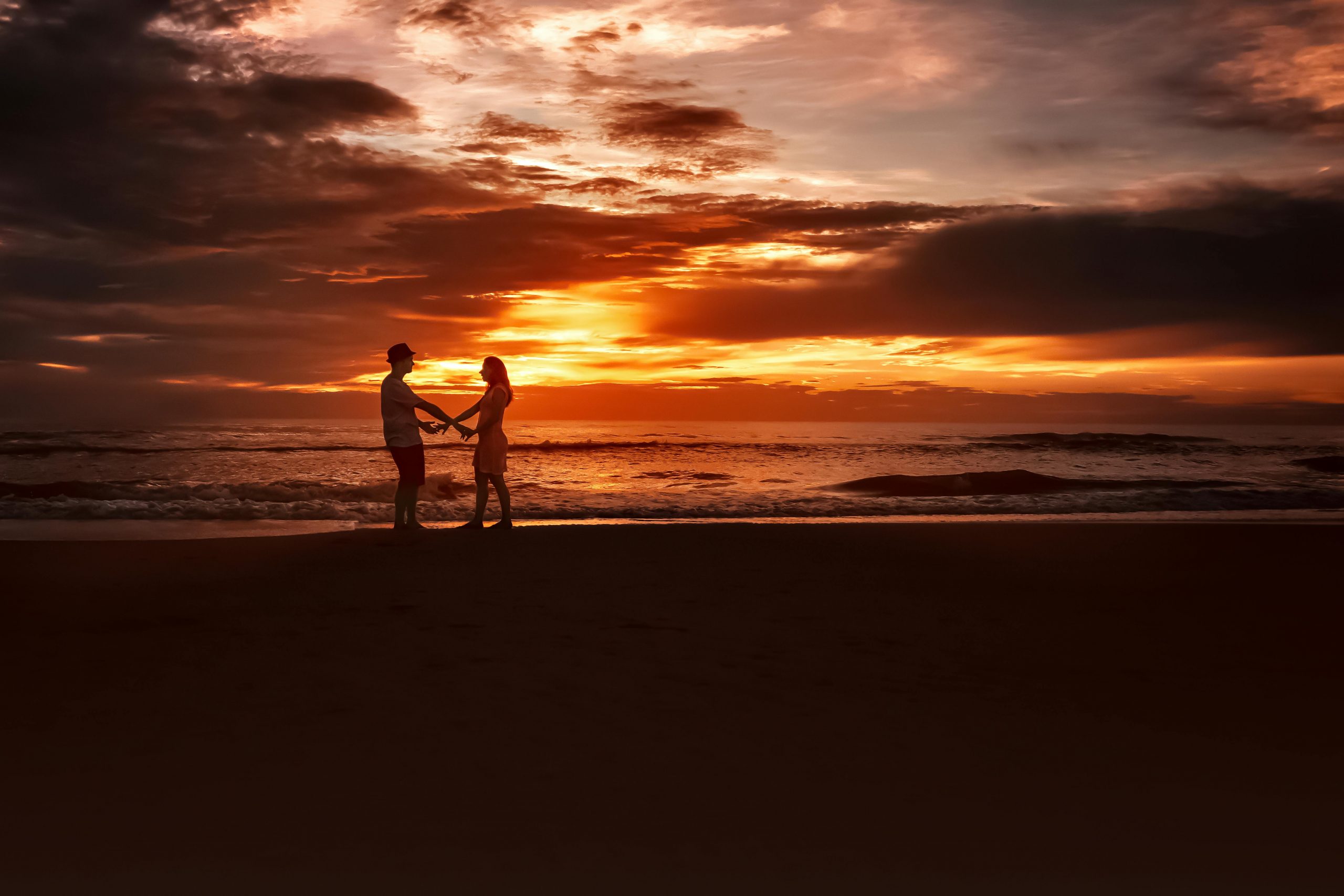 Silhouetted couple holding hands on the beach at sunset, showcasing romance and tranquility.